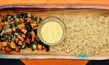 A wooden tray with rice, vegetables and sauce.
