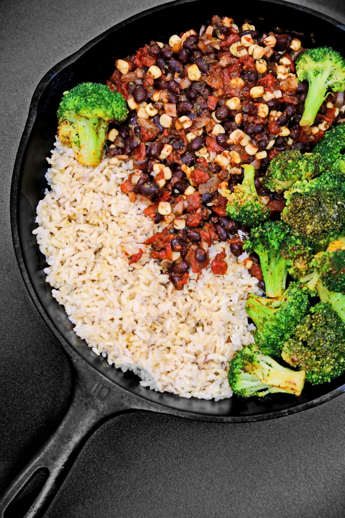 A pan of rice, beans and broccoli with some meat.